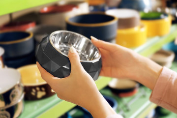 Hands of young woman selecting bowl in pet shop, close up view
