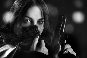 woman in leather coat with gun on dark blurred background, monochrome image
