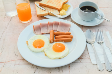 Breakfast with Fried egg, Ham, Sausage, toast, jam, butter, water melon, orange juice and black coffee on marble table.