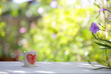 White cup whit heart pattern and plants on wooden table