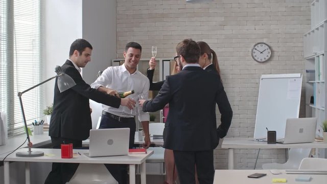 Group of cheerful colleagues pouring champagne and drinking in the office