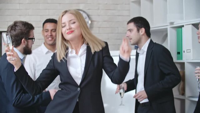 Beautiful business lady dancing with champagne flute with her colleagues in the office