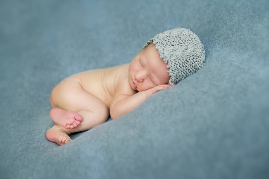 Newborn baby boy sleeping in the fetal position on a blue backgr