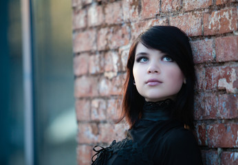 Close up portrait of gothic teenager girl on wall bricks background  

