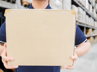 Delivery man in blue uniform holding the box on warehouse blurre