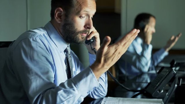 Angry businessman with documents and laptop talking on phone in office 
