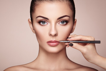 Beautiful woman paints lips with lipstick. Beautiful woman face. Makeup detail. Beauty girl with...