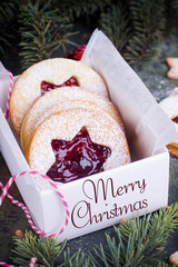 Christmas or New Year homemade sweet present in white box. Traditional Austrian christmas cookies - Linzer biscuits filled with red raspberry jam. Festive decoration. Text Merry Christmas
