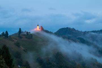 Jamnik church on a hillside in autumn, foggy weather at sunset in Slovenia