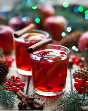 Drink on winter evening. Hot granberry orange pomegranate punch or mulled wine, sangria in a rustic wooden table. Christmas tree decorations.