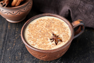 Masala tea chai latte traditional hot Indian sweet milk spiced drink, ginger, fresh spices blend organic infusion healthy wellness beverage in rustic clay cup on dark table background