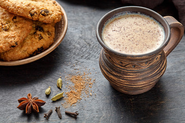 Fototapeta na wymiar Masala pulled tea chai latte traditional hot Indian sweet milk spiced drink, ginger, cinammon sticks, fresh spices blend, anise organic infusion healthy wellness beverage in rustic clay cup