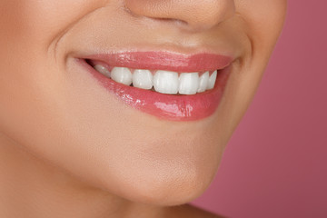 Beautiful smile with whitening teeth. Dental photo. Macro closeup of perfect female mouth, lipscare. Perfect pink lip makeup. Perfect clean skin, light fresh lip make-up. Pink background