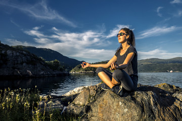 Young woman enjoying the sunny day on the rocks next to the fjor