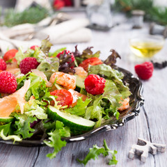 Fresh salad with smoked salmon, shrimps, raspberries and cherry tomatoes on white wooden background. Delicious Christmas themed dinner table
