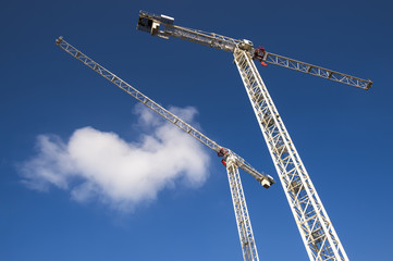 Modern hi-rise construction site with cranes towering into bright blue sky with puffy white clouds