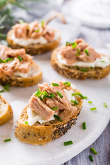 Slices of baguette with fresh tuna, cream cheese and chopped onion chives on marble board. Christmas themed dinner table.