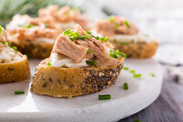 Slices of baguette with fresh tuna, cream cheese and chopped onion chives on marble board. Christmas themed dinner table.