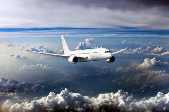 Fototapeta White passenger wide-body plane. Front view. Aircraft is flying in blue cloudy sky.