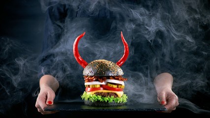 Devil burger with bacon and vegetables on black slat plate in wo