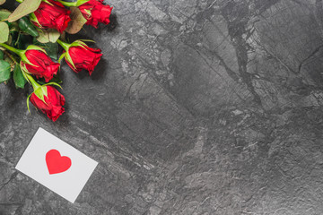 Red roses  and message card on black marble board. Valentines Day background, wedding