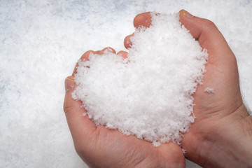 Man holding with both hands a snowball shaped like a heart against the a background of white snow