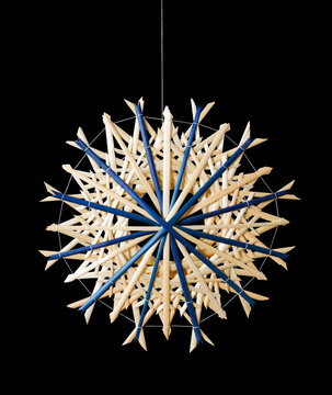 Blue straw star Christmas decoration on black background. Handmade decor for windows, as gifts or to hang on the xmas tree, traditionally made from natural straw. Macro photo front view close up.