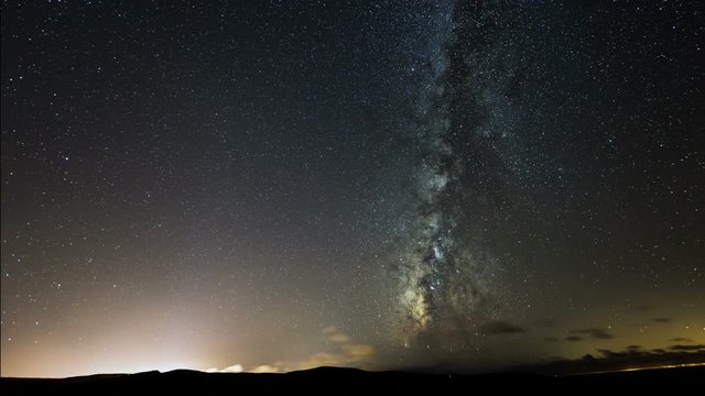 A time lapse shot of the milky way at night with a city light and some clouds. 11100
