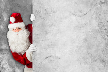 Santa claus hiding and looking through behind empty concrete billboard wall 