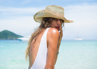 Closeup portrait of prettty brunette woman in sexy white swimsuit and straw hat standing in the water against beautiful lagoon sea and sky background