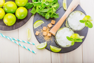 Two fresh mojitos cocktail on wooden background. Mojitos with mint leaves, lime and ice. Drink making tools and ingredients for cocktail. View from above.  