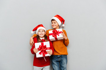 Two happy children in santa claus hats holding present boxes