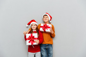 Two funny children in santa claus hats with gift boxes