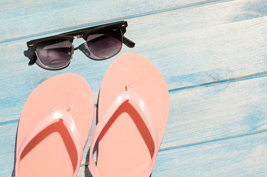 pink flip flops and sunglasses on blue wooden table with sunlight
