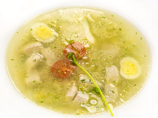 Broth with pasta greens and quail egg in a white plate