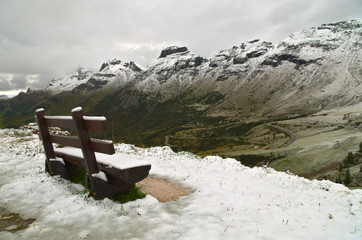 Passo Pordoi: bench covered by the first snow of the season on the Dolomiti mountains 
