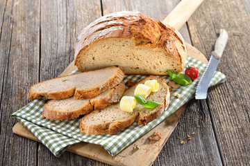 Frisches Steinofenbrot mit Butterröllchen auf einem altem Backbrett serviert - Fresh stone oven...