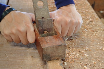 Hand of worker planing a plank of wood using a hand planer