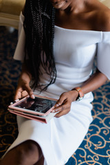 black woman in white dress. she is taking a device in her hands chatting in internet. Blue carpet...