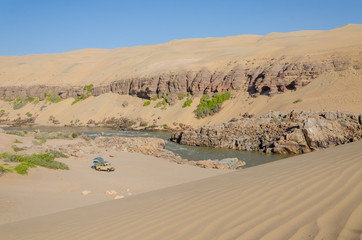 Fototapeta na wymiar Offroad camping at Kunene River in front of towering ancient Namib Desert sand dunes of Namibia and Angola
