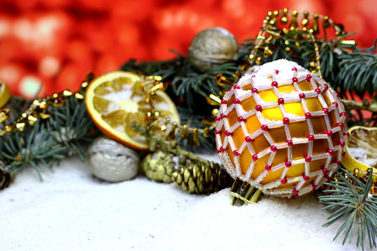 Christmas red background with a beads decorated gold ball, dry oranges fruit, fir brunch in snow