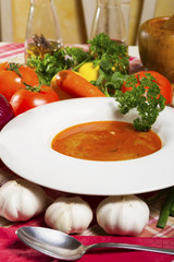 Red fish soup in a white plate beside fresh vegetables.