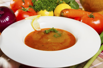 Red fish soup in a white plate beside fresh vegetables.