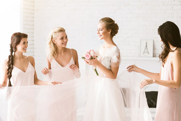 Smiling bridesmaids holding the dress of the bride