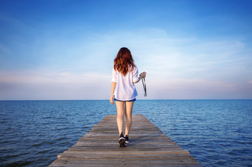 Woman walking on wooden bridge extended into the sea.