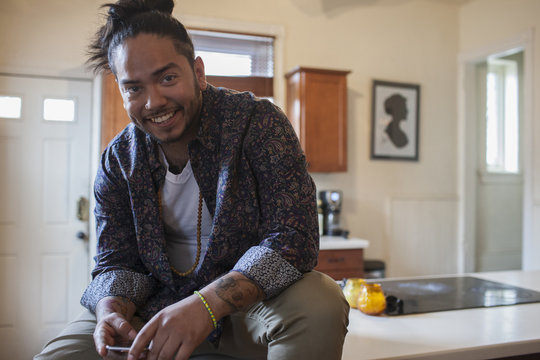 Portrait of smiling young man sitting on kitchen countertop