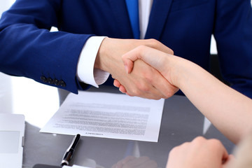 Businessman and business woman shaking hands to each other above signed contract