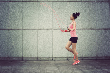 Fototapeta na wymiar young fitness woman rope skipping against city wall