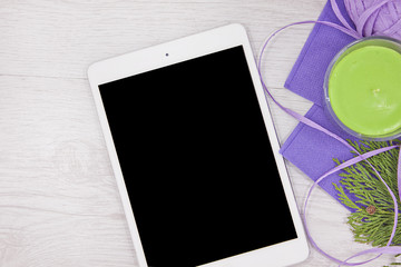 Tablet with green apple aromatic candle, lilac ribbon and cypress on white wood background 