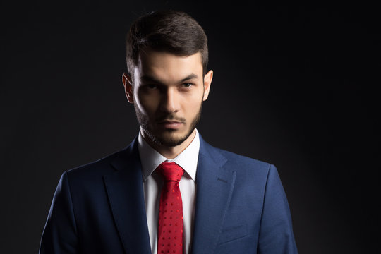 Strict businessman in suit with red tie on black background